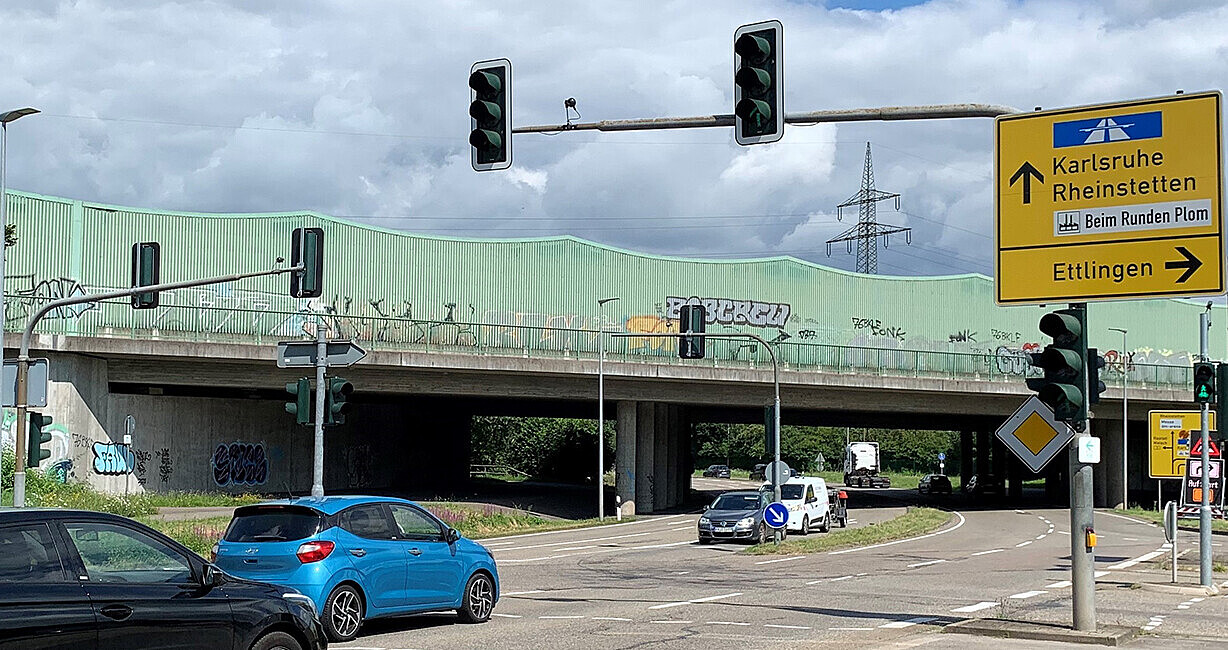 Fahrzeuge an Straßenkreuzung mit Ampeln und Straßenverkehrsschildern mit Blick auf den Einmündungsbereich L 607 und Mörscher-Straße, im Hintergrund Überführung der A 5