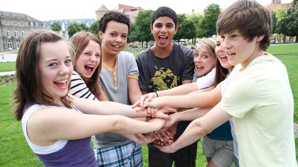 Jugendliche Mädchen und Jungs fassen sich an den Händen und lachen in die Kamera