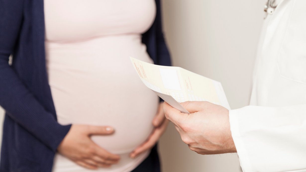 Ein Arzt übergibt einer schwangeren Frau eine Krankmeldung