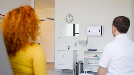 Ein Orthoptist und eine Patientin vor einer Buchstabentafel