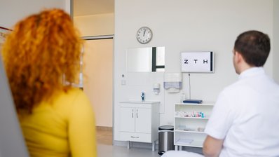 Ein Orthoptist und eine Patientin vor einer Buchstabentafel