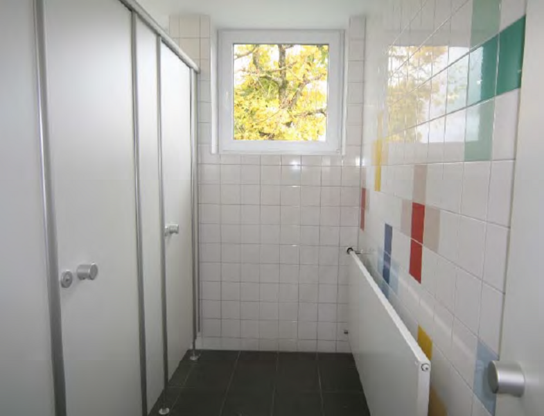 Sanierung Grundschule Feldhausen - Blick in die Toilette, mit neuen weißen und bunten Kacheln und neuen sanitären Anlagen